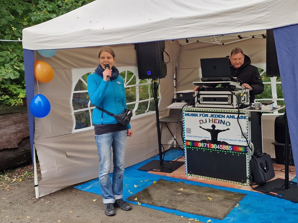 Ortsteilbürgermeisterin begrüßt Gäste zur Feier, unterstützt von DJ Heino, der Musik aus den letzten 100 Jahren zu Gehör brachte